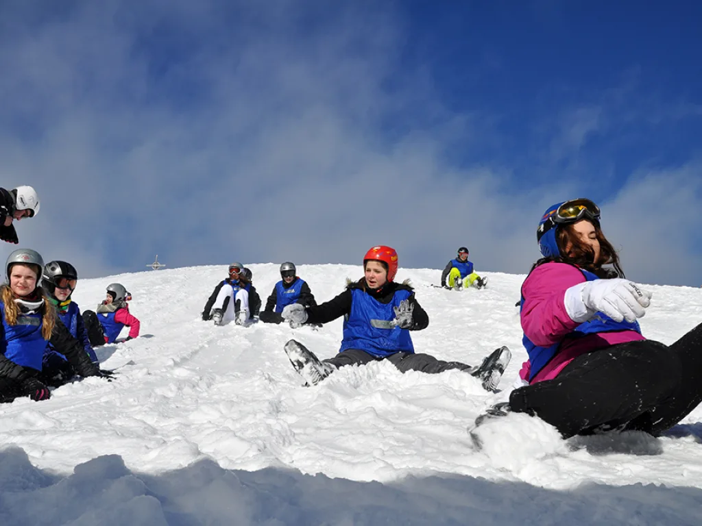 Jugendliche liegen und sitzen im Schnee, darüber blauer Himmel.